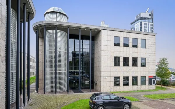 Modern kantoorgebouw aan de Rivium Westlaan 19 met glazen gevelpartijen en pilaren, met een auto geparkeerd voor de ingang.